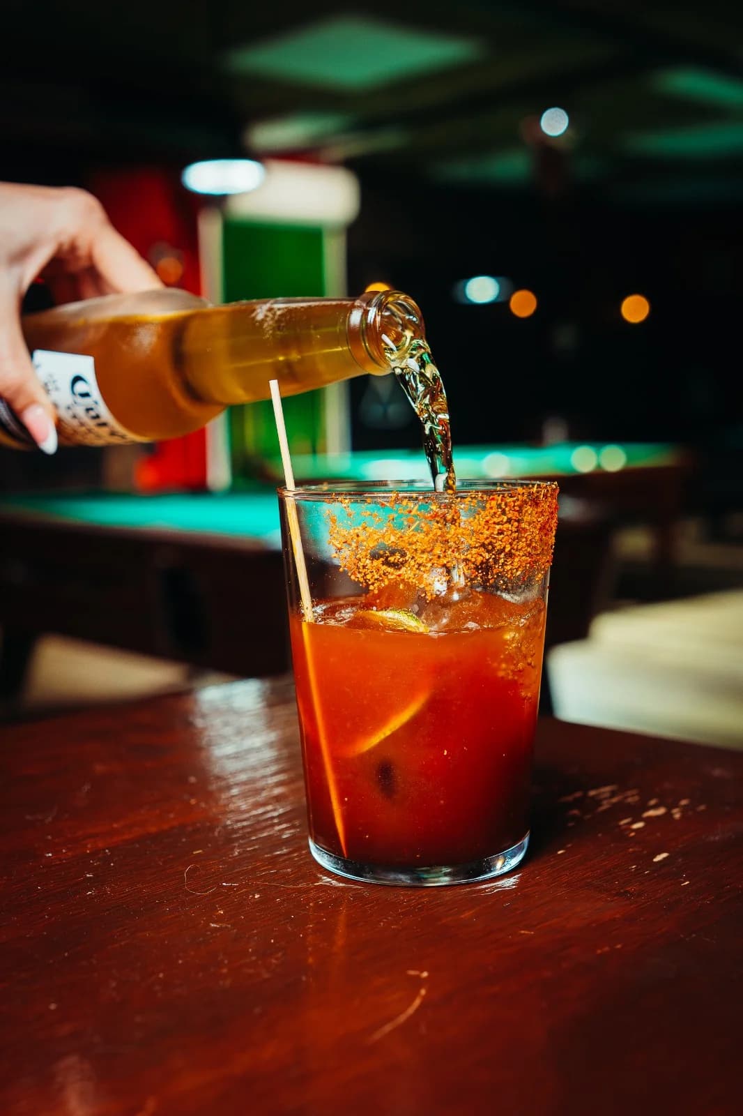 Bartender preparando michelada con mesas de billar al fondo