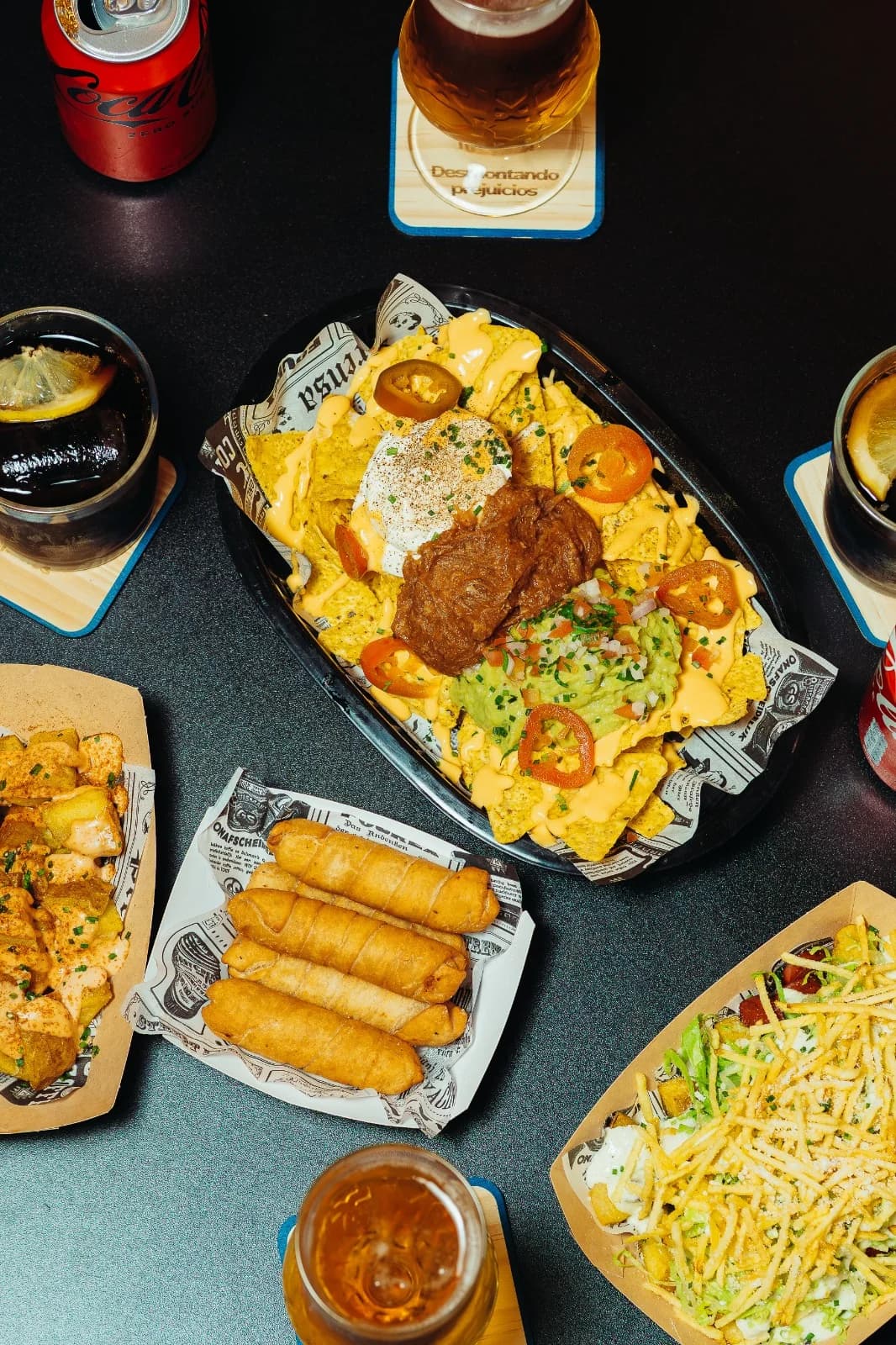 Mesa con nachos, cócteles y aperitivos en Singular Pub